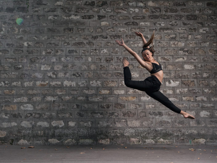 danseuse qui saute devant un mur de pierre vers la gare de bercy