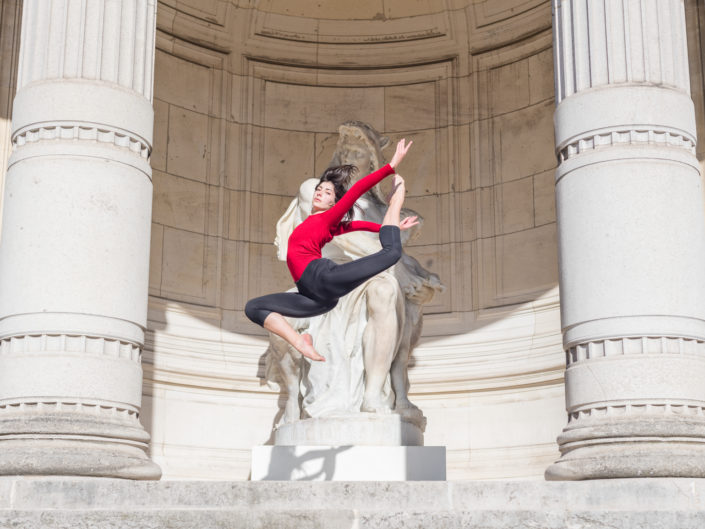 gymnaste faisant un saut avec un justaucorps rouge devant 2 colonnes